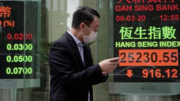 Мужчина в защитной маске на фоне табло с котировками ценных бумаг в Гонконге 