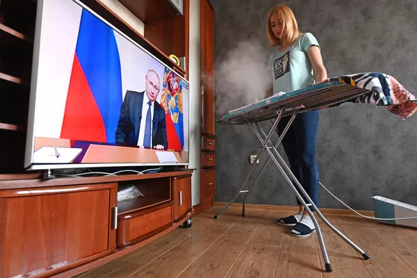 Женщина гладит белье и смотрит трансляцию обращения президента России