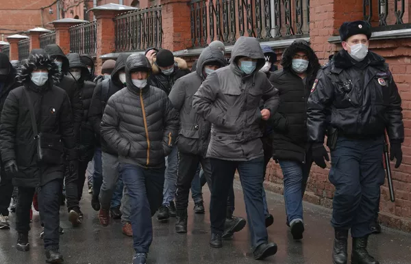 Сотрудник полиции выстраивает в очередь мигрантов у здания УФМС в Санкт-Петербурге