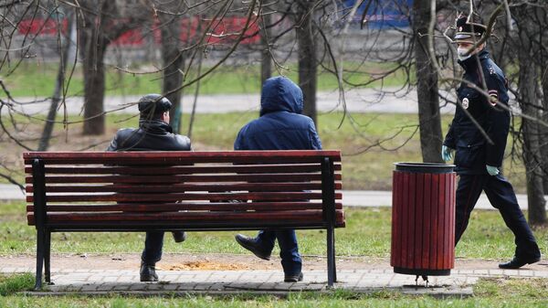 Сотрудник полиции подходит к людям, сидящим на скамейке в сквере Сотрудник полиции подходит к людям, сидящим на скамейке в сквере
