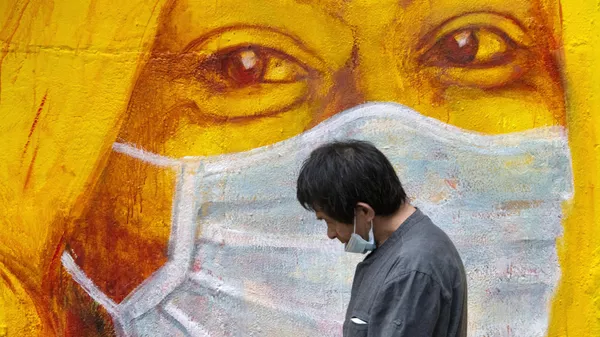 Прохожий около стены с изображением человека в маске в Гонконге