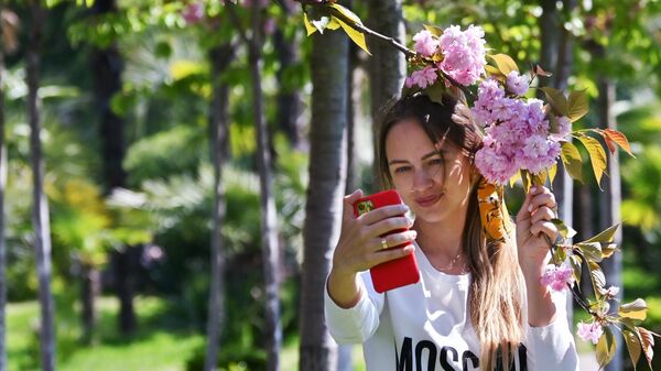 Девушка фотографируется на мобильный телефон на аллее Черешневый сад в Сочи Девушка фотографируется на мобильный телефон на аллее Черешневый сад в Сочи