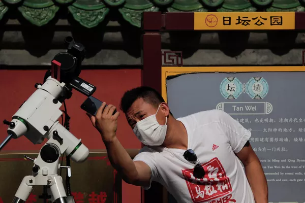 Мужчина снимает  солнечное затмение в Пекине, КНР