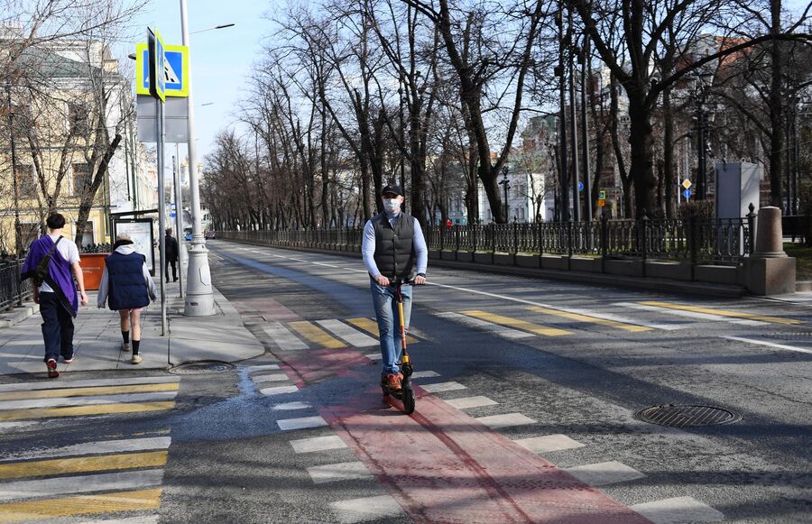 Мужчина в медицинской маске едет на самокате по велодорожке в центре Москвы. Мужчина в медицинской маске едет на самокате по велодорожке в центре Москвы.