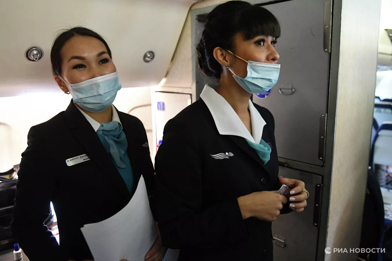 two women wearing masks and standing in an airplane