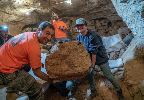 Археологи держат древнюю корзину, извлеченную из пещеры Мурабаат в Иудейской пустыне близ Мертвого моря 30 января 2021 года