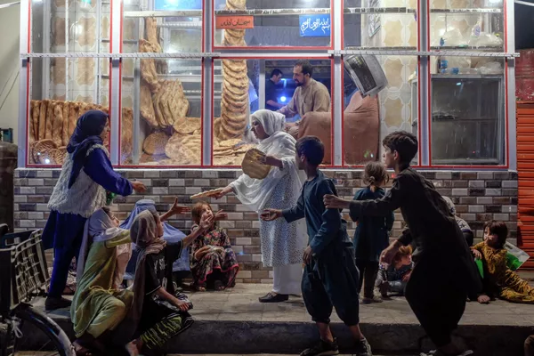 Женщина раздает хлеб нуждающимся возле пекарни в Кабуле