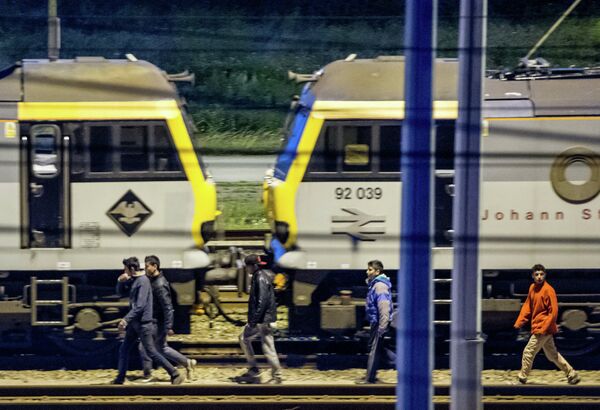 Мигранты идут вдоль железнодорожных путей в терминале Евротуннеля Мигранты идут вдоль железнодорожных путей в терминале Евротуннеля