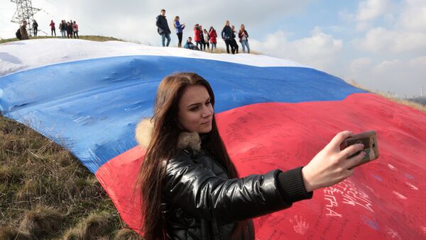 Девушка делает селфи на фоне огромного флага России на фестивале Крымская весна в селе Мирное Симферопольского района Республики Крым Девушка делает селфи на фоне огромного флага России на фестивале Крымская весна в селе Мирное Симферопольского района Республики Крым