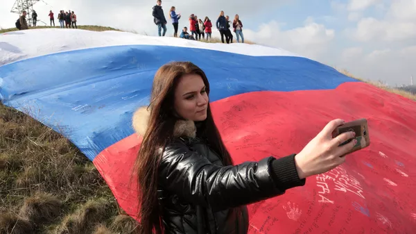Девушка делает селфи на фоне огромного флага России на фестивале Крымская весна в селе Мирное Симферопольского района Республики Крым Девушка делает селфи на фоне огромного флага России на фестивале Крымская весна в селе Мирное Симферопольского района Республики Крым