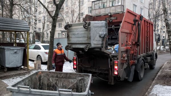 Сотрудник коммунальных служб выгружает мусор из контейнера в мусоровоз Сотрудник коммунальных служб выгружает мусор из контейнера в мусоровоз